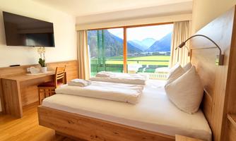 A bright and modern bedroom with a large window that showcases an impressive mountain landscape. It is furnished with wooden furniture and offers a cozy atmosphere.