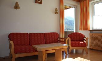 A cozy living area with a red upholstered sofa and a matching armchair. Large windows offer a view of the mountains.