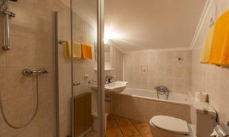 A modern bathroom with a shower and a bathtub. Yellow towels hang on the wall, and the floor is tiled.