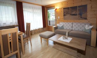 A cozy living room with wood paneling, a comfortable sofa, and a wooden table. Large windows provide plenty of natural light and an inviting atmosphere.