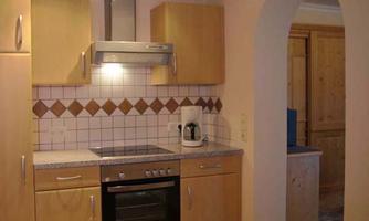 A modern kitchen with wooden furniture and white tiles. It is equipped with a stove, a refrigerator, and a microwave.