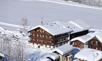 A picturesque snowy village with traditional wooden buildings. The landscape is calm and wintry, ideal for a winter sports holiday.