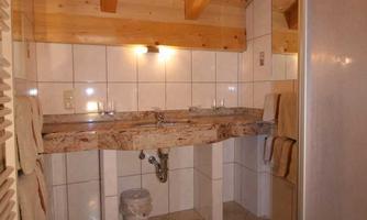 A modern bathroom with a wooden ceiling and bright tiled floor. It features a wooden sink and a shower cubicle.