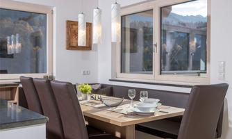 A modern dining area with a wooden table and elegant chairs. Large windows offer a view of the mountains.