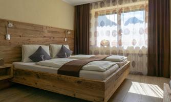 A modern bedroom with a large wooden bed and comfortable pillows. Large windows let in plenty of daylight and provide a view of the outdoor area.