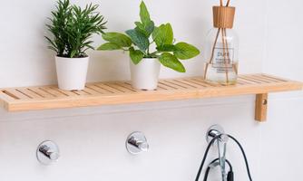 A wooden shelf with two small plants and a room scent is attached to the wall. Below it, two hooks hang, one of which has a hairdryer attached to it.