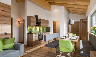 A modern kitchen with wooden shelves and a dining table. The room has high ceilings and large windows that let in plenty of light.