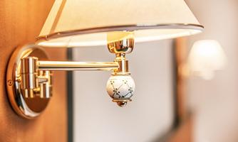 An elegant wall lamp with a gold arm and a lampshade. The lamp has a decorative element with a pattern.