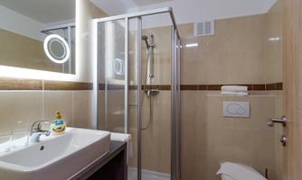 A modern bathroom with a shower and sink. The walls are in light shades and there is a large mirror light.