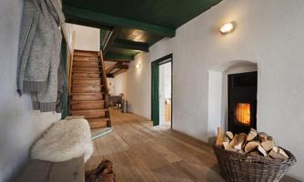 A cozy entrance area with a wooden staircase and a fireplace. A basket with logs is ready to feed the fire.