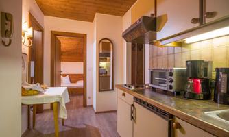A cozy kitchen with wooden paneling and modern appliances. In the background, a bedroom can be seen.