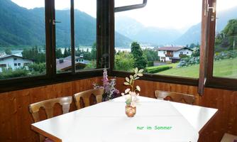 A cozy room with a window view of a green landscape and mountains. Flowers are on the table, and it feels welcoming and friendly.