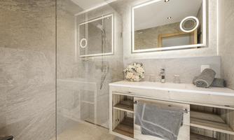 A modern bathroom with a spacious shower and elegant tiles. Flowers and towels are placed on the sink countertop, creating a peaceful atmosphere.