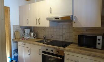 A modern kitchen with bright cabinets and stainless steel appliances. It is well-equipped with a stove, microwave, and kitchen utensils.