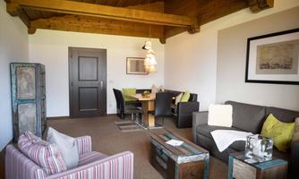 A cozy living space with a wooden beam ceiling. The furnishings include a sofa, a dining area, and various decorative elements.