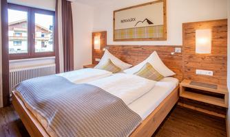 A cozy bedroom with a double bed and wooden furniture. The room has large windows and a friendly atmosphere.