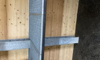 A metal shelf with a sturdy grid bottom in a wooden room. There is a box on the shelf.