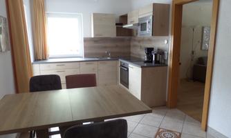 A modern kitchen with a dining table and chairs. Bright colors and plenty of daylight characterize the space.