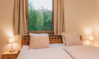 A cozy bedroom with two beds and warm light. A beautiful mountain landscape can be seen through the window.