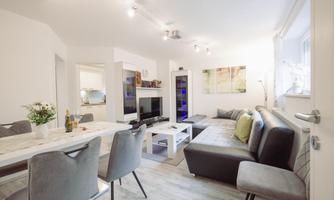 A modern living room with a cozy couch and a dining table. There is a television and bright, inviting colors that create a pleasant atmosphere.