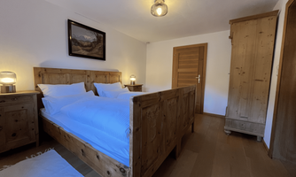 A cozy bedroom with wooden beds and bright light. The walls are plain, and a picture adds a pleasant atmosphere to the room.