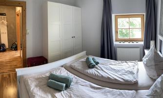 A bright bedroom with two beds, fresh towels, and a window that overlooks the garden view. In the background, an open room with a wardrobe is visible.
