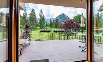 A beautiful balcony overlooking a green meadow and mountains. In the background, there are trees and a clear sky.