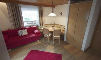 A cozy living room with a red couch and a dining area. The room has a wooden floor and large windows that let in a lot of light.