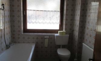 A bathroom with a bathtub, a toilet, and a window. The walls are decorated with a patterned tile covering.