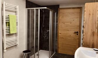 A modern bathroom with a glass shower and a wooden vanity. On the wall hangs a towel rack with a green towel.