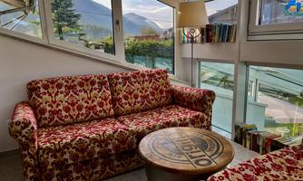 A cozy living room with a red and white sofa and a round table. Large windows offer a view of the surrounding landscape.