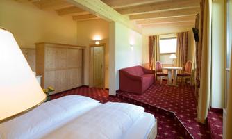 A cozy hotel room with a double bed, a sofa, and a table. The warm colors and wooden elements create an inviting atmosphere.