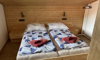 A cozy bedroom with two single beds and wood paneling. On the beds are striped blankets and colorful towels.