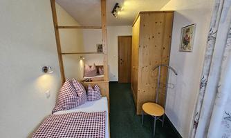A cozy room with two beds, striped pillows, and a wooden wardrobe. The walls are bright, and the floor is green.