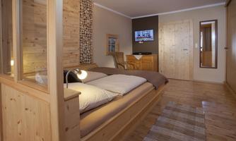 A modern bedroom with wooden details, a large bed, and a television on the wall. The room is bright and inviting, ideal for relaxed nights.