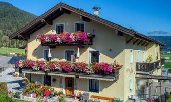 A charming, blooming house with several balconies and colorful flowers. The surroundings are enveloped by picturesque mountains.