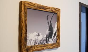 A framed black-and-white photo of a ibex on a mountain peak. The frame is made of rustic wood.
