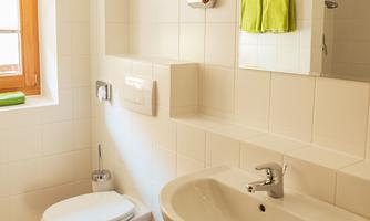 A modern bathroom with a bright tiled floor. There is a sink, a toilet, and green towels.