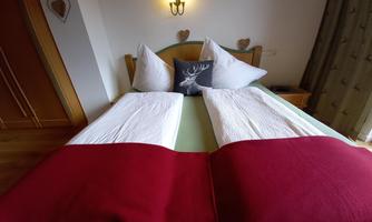 A cozy bedroom with a double bed, dressed in white sheets and red blankets. Decorative elements hang on the wall, creating a warm atmosphere.