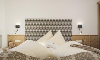A cozy bedroom with a padded headboard and large pillows. Modern night lights are installed on the walls.