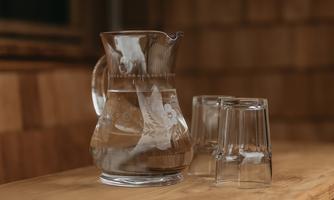 A jug of water is on a wooden table. Next to it are two glasses.