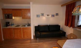 A cozy apartment with a wooden kitchen and a black sofa. In addition, there is a dining table with chairs that complements the living atmosphere.