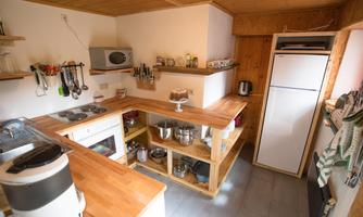 A modern, well-equipped kitchen with wooden shelves and beige walls. The work surface is tidy and the appliances are conveniently arranged.