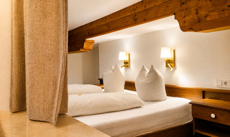 A cozy bedroom with two beds and large pillows. The walls are kept neutral and there is pleasant light from the wall lamps.