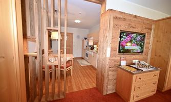 A cozy living space with wooden elements and a separate dining area. In the corner is a modern kitchen and a television on the wall.