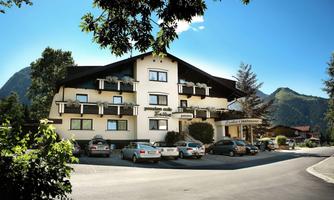 A cozy hotel with several windows and a balcony.  
Surrounded by mountains and trees, with parking available at the front door.