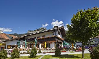 A cozy restaurant with a terraced outdoor area and shady umbrellas. In the background, there are mountains and a blue sky.