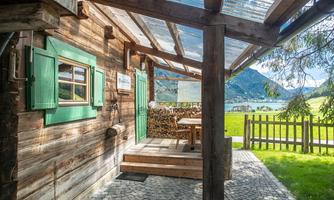 A cozy wooden cabin with green shutters and a beautiful view of nature. Outside there is a table and chairs to enjoy the surroundings.