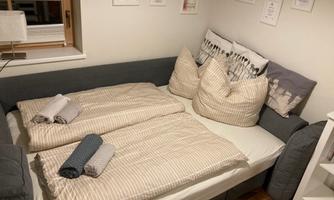 A cozy bedroom with a gray sofa bed. There are pillows, blankets, and towels on the bed, as well as some pictures on the wall.
