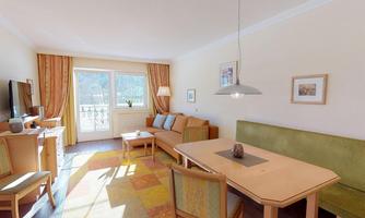 A bright living room with a cozy sofa and a dining table.  
Large windows provide plenty of daylight and a pleasant atmosphere.